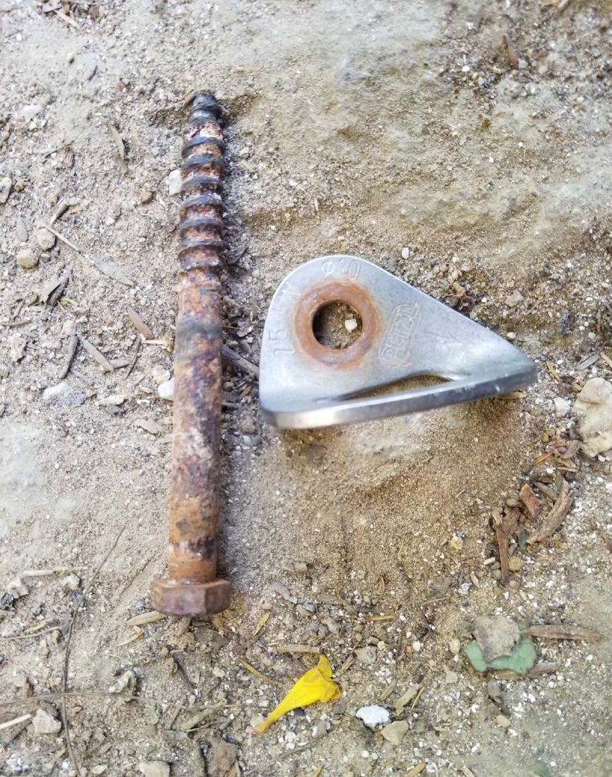 A long rusted tapered bolt beside an old hanger, lying on the ground